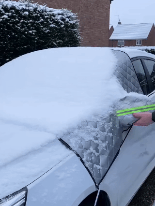 Lifting the windshield cover to remove the snow resting on it